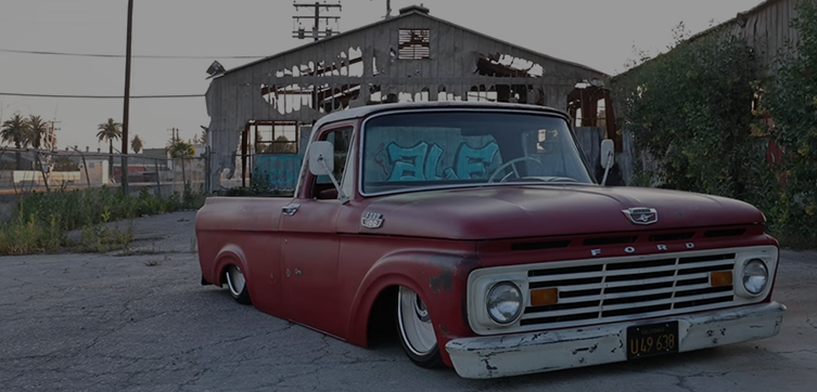 Slammed classic Ford F100 truck with patina finish parked in front of an abandoned warehouse — custom automotive performance build