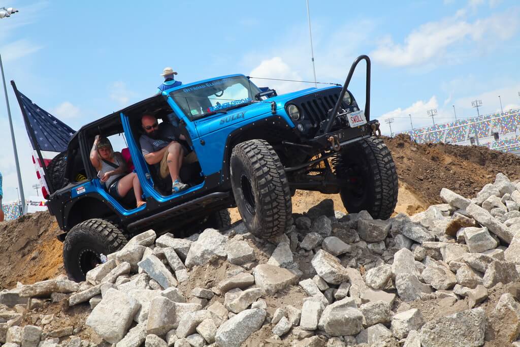 People Hold On to Handles as Bright Blue Jeep Drives Over a Pile of Rocks