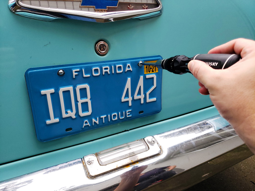 Unscrewing the license plate from a 1957 Chevrolet 210 decklid