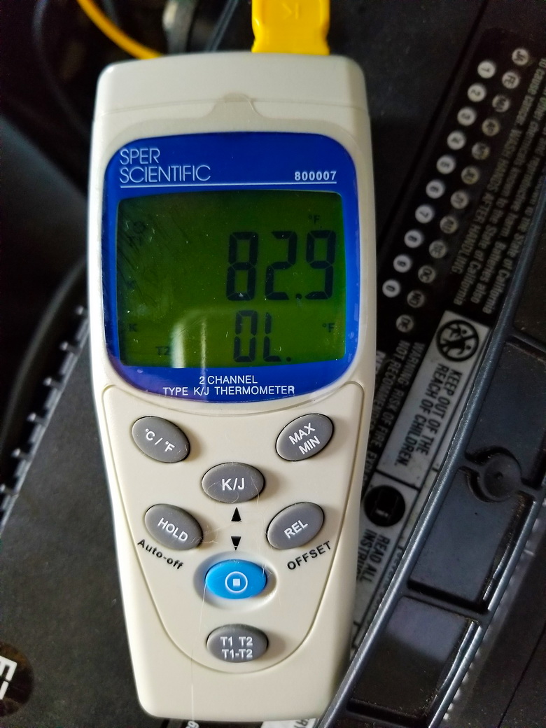 A digital thermometer takes a heat reading off of car engine fuel lines installed without fuel line protective sleeves.