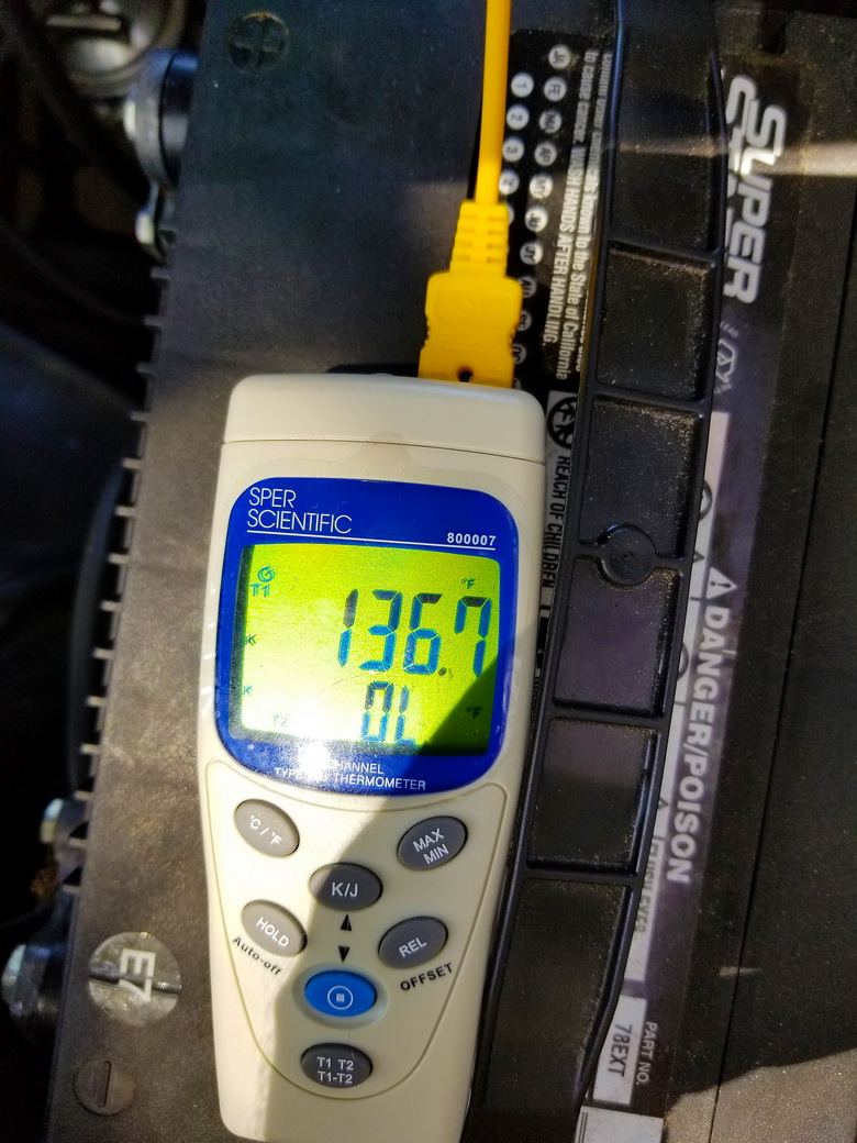 A digital thermometer takes a reading off a car engine installed without fuel line protective sleeves.