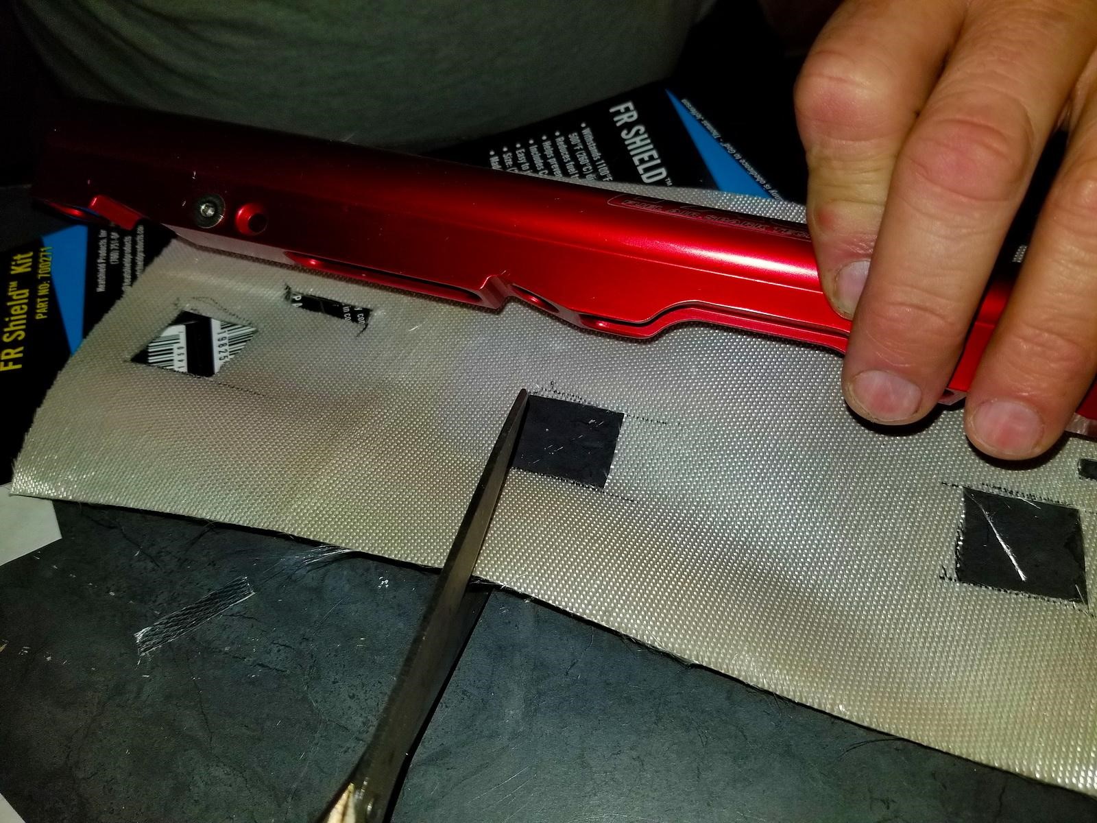 A man cuts a hole in fuel line insulation while holding against a fuel rail. 