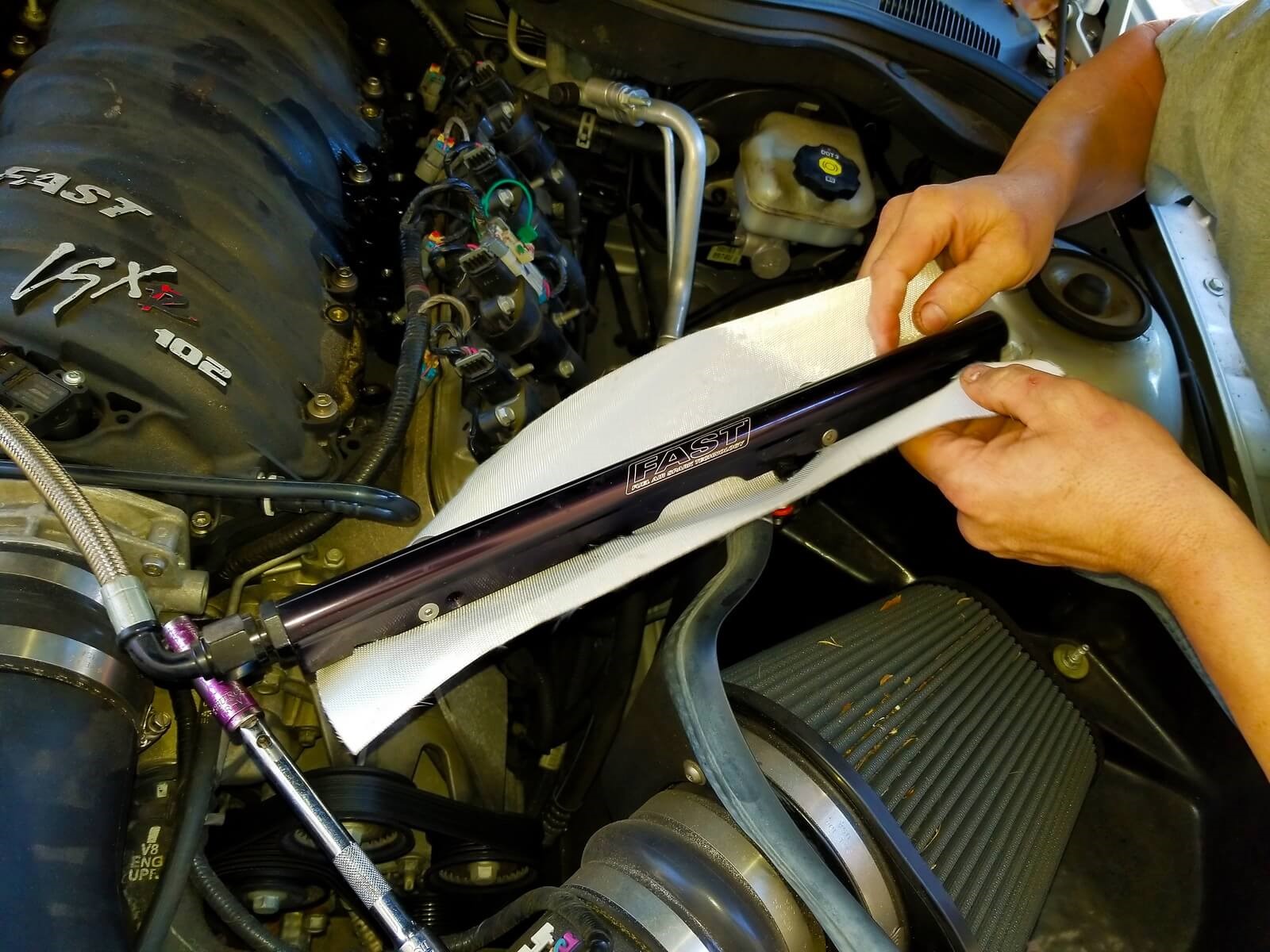 A man wraps fuel line insulation around a fuel rail.