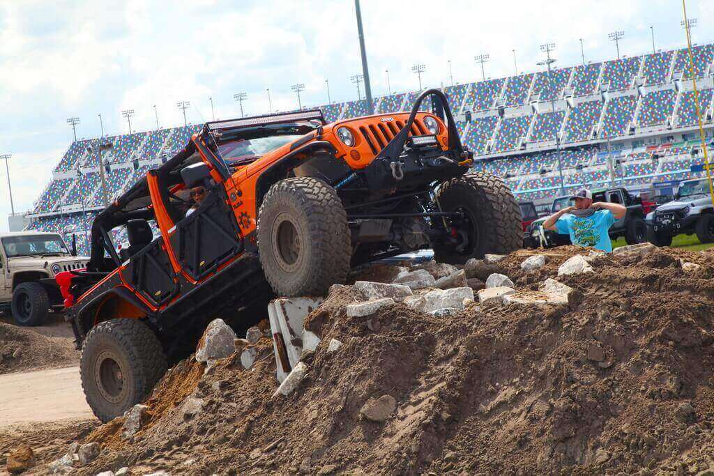 Orange Jeep Drives Over Rocky Mound of Dirt