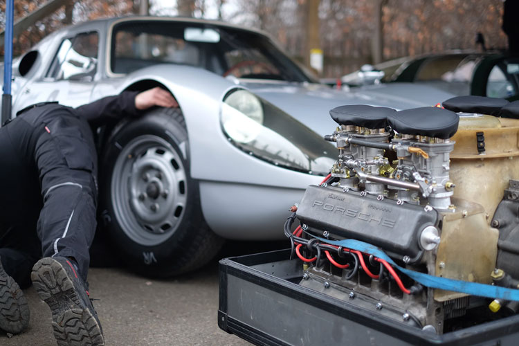 A man leans under his car as he works on how to install exhaust wrap