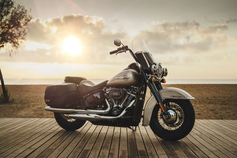 A gray motorcycle parked on an ocean boardwalk against a setting sun