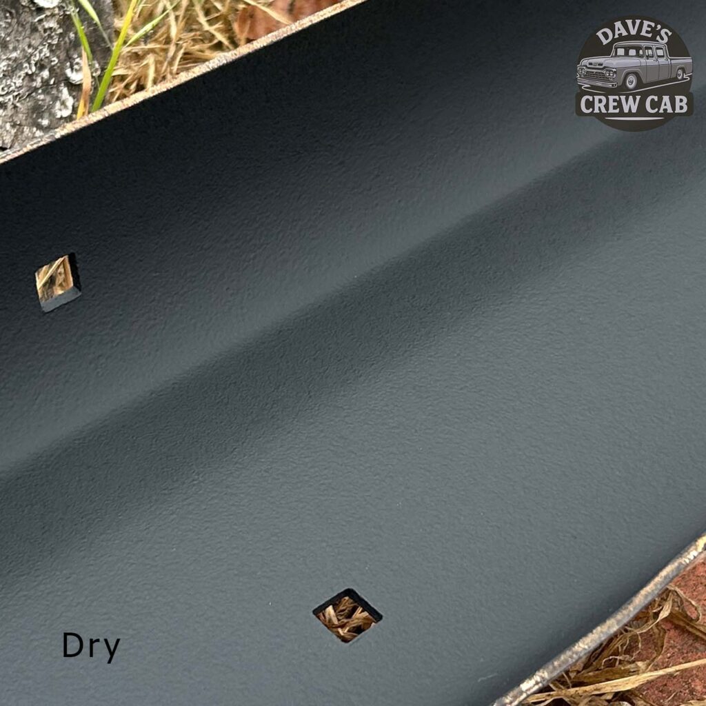 Close-up of a dark, textured metal surface with two square holes, a few dry leaves inside, and the word Dry in the corner. Daves Crew Cab logo is visible in the top right corner. Grass and gravel are at the edge.