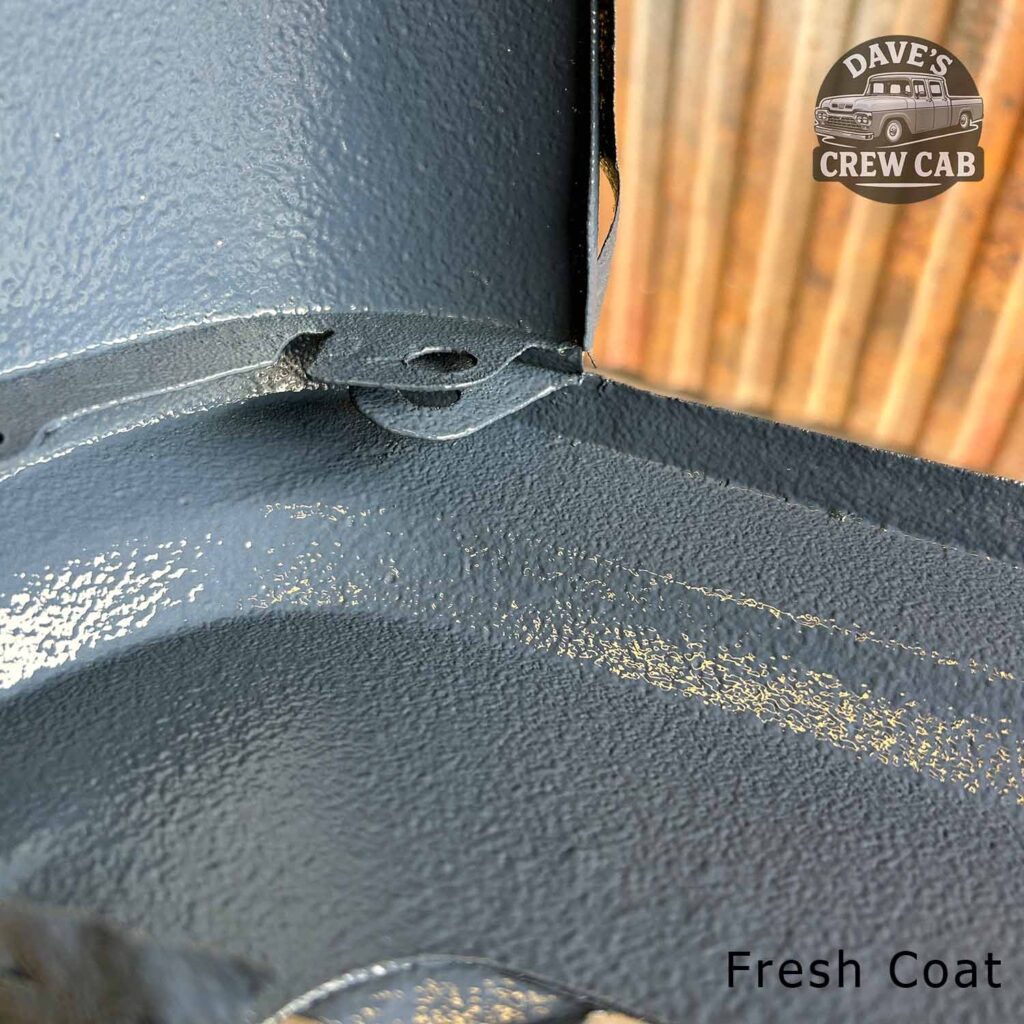 Close-up of a textured gray painted metal surface next to a piece of wood. The “Dave’s Crew Cab” logo is in the top right corner, and the text “Fresh Coat” appears in the bottom right corner.