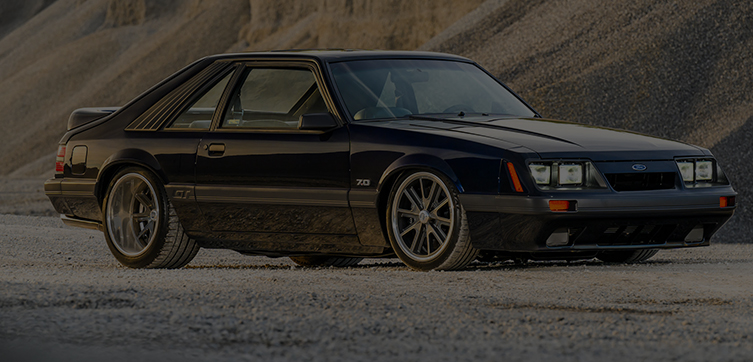 Black classic Ford Mustang parked on gravel with custom wheels and lowered stance