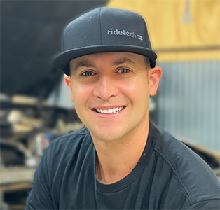 Man wearing a black Ridetech hat smiling in a workshop setting